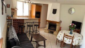 En stue med sofa, stole, et lille bord, en pejs og et spiseområde med bord og stole.