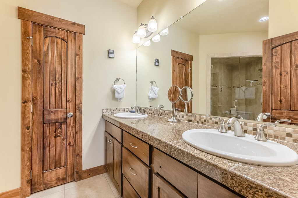 A bathroom with two sinks, wooden cabinets, a large mirror, and a shower area.