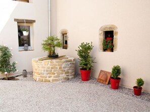Un espace extérieur aménagé en pierre, agrémenté de plantes en pot et d’un petit banc en pierre.