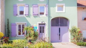 Un edificio de dos plantas con fachada verde clara, contraventanas moradas y una entrada central en arco.