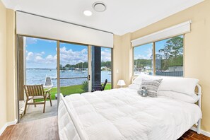 A bedroom with a large bed, a chair, and a view of a body of water through a sliding glass door.