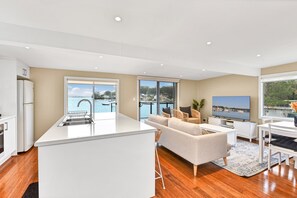 A modern kitchen with a central island, a dining area with a TV, and a view of a marina.