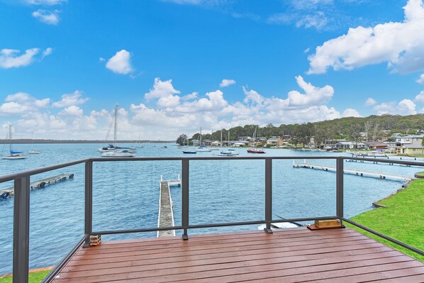 A wooden deck with a railing overlooking a marina with boats and a distant bridge.