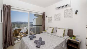 Una camera d'albergo con un balcone, un letto con asciugamani, un comodino e opere d'arte alle pareti.