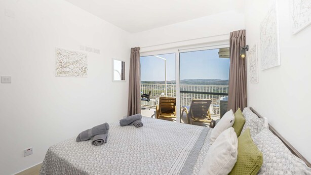 Un dormitorio con cama, vista al balcón y una ventana.