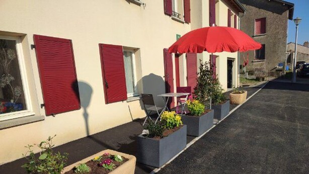 Un bâtiment avec des volets rouges, des tables et chaises à l’extérieur et des plantes en pot.