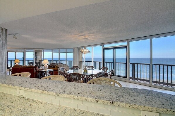 Enjoy ocean views from the expansive windows, a central dining area, and a balcony with a railing.