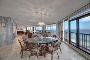 Un comedor amplio con una mesa de vidrio y sillas de mimbre, ventanas grandes con vista al mar y una decoración interior moderna.