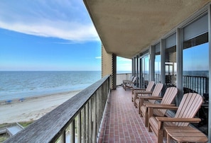 Enjoy the ocean view from this balcony with a clear view of the beach, featuring Adirondack chairs and a tiled floor.