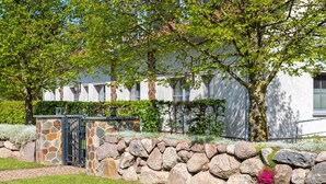 A stone wall with a gate, a paved path, and a building with a white facade and windows. - (2) Barbara, 3-room apartment, wheelchair accessible, ground floor - Ostseeferienhaus (Am Salzhaff)