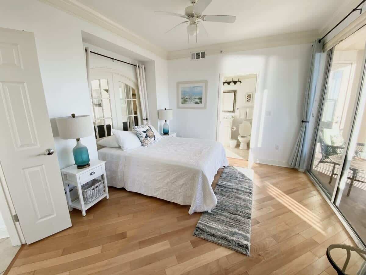 A bedroom with a bed, bedside tables, a ceiling fan, and a view through a glass door.