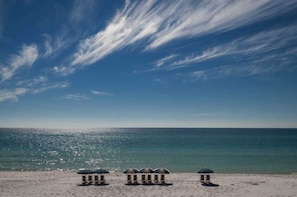 Uma praia com três estruturas em formato de cúpula, provavelmente para relaxamento ou refeições, e uma vista desobstruída do oceano.