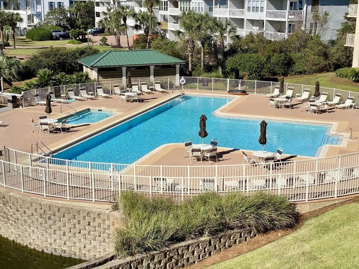 A rectangular pool with a white fence, lounge chairs, and umbrellas.