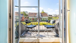 A balcony with two chairs, a glass door, and a view of a residential area. - (7) Lisa, 2-room apartment, loggia, upper floor - Ostseeferienhaus Drachenflieger Pepelow OFC (Am Salzhaff)