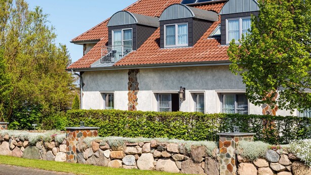 A two-story house with a stone wall, a stone pillar, and a solar panel on the roof. - (7) Lisa, 2-room apartment, loggia, upper floor - Ostseeferienhaus Drachenflieger Pepelow OFC (Am Salzhaff)
