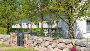 A stone wall with a gate, a paved path, and a building with a white facade and windows. - (7) Lisa, 2-room apartment, loggia, upper floor - Ostseeferienhaus Drachenflieger Pepelow OFC (Am Salzhaff)