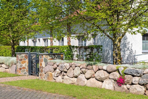 A stone wall with a gate, a paved path, and a building with a white facade and windows.