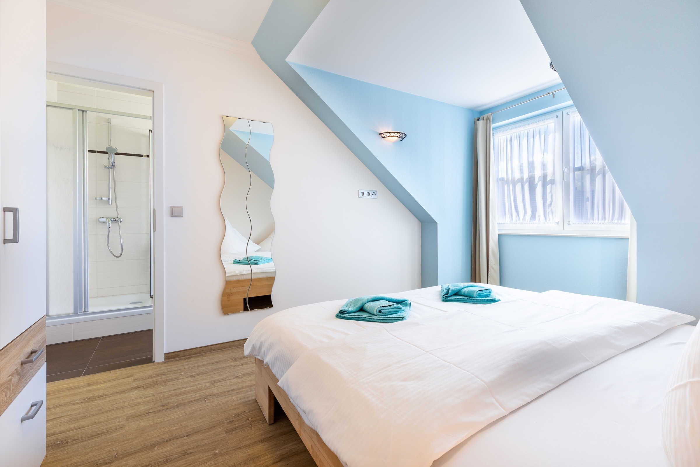 Een moderne slaapkamer met een schuine kap, een glazen douche, een bed met witte lakens en uitzicht op de omgeving.