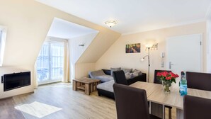Una sala de estar moderna con sofá, mesa de centro y mesa de comedor. Hay un televisor montado en la pared, una ventana con cortinas y una puerta.