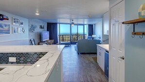 A spacious room with a kitchen area, a dining table, and a large window offering a view of the ocean.