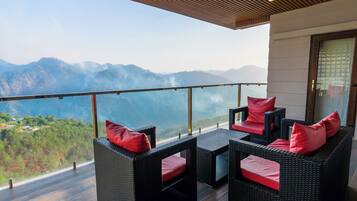 Un balcon agrémenté de meubles en osier et de coussins rouges, offrant une vue sur un paysage montagneux.