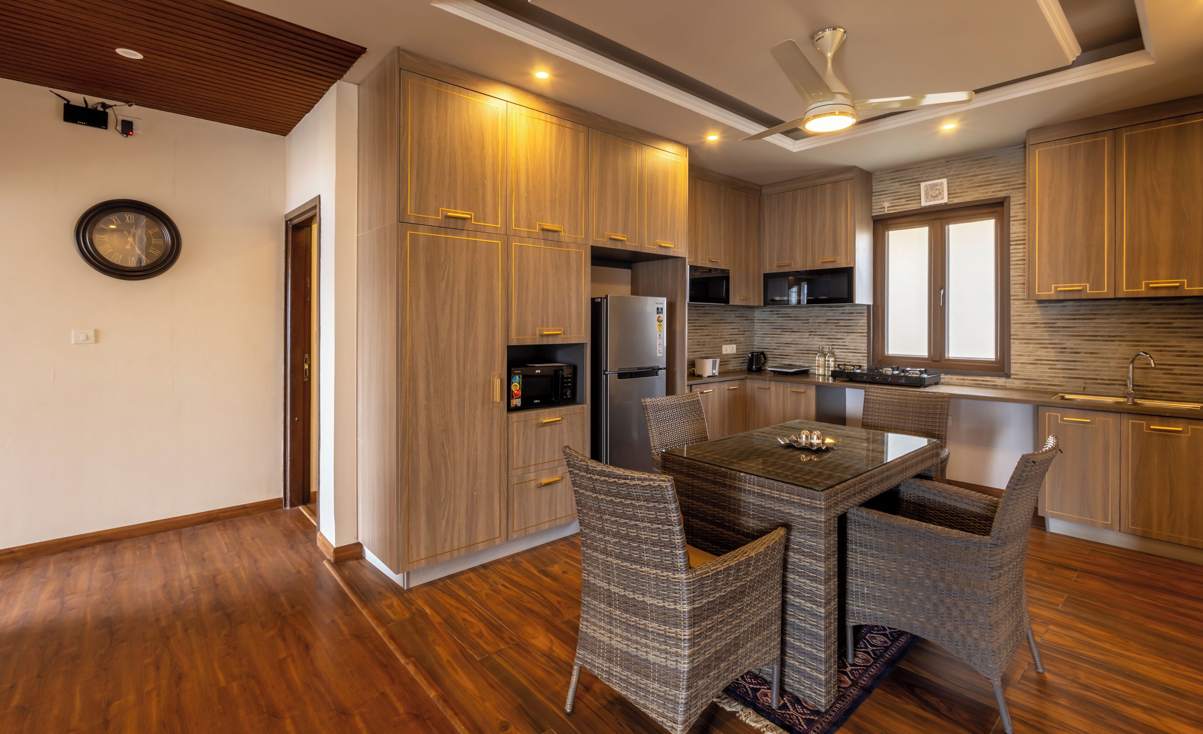 A modern kitchen with wooden cabinets, a stainless steel refrigerator, a microwave, and a dining area with wicker chairs.