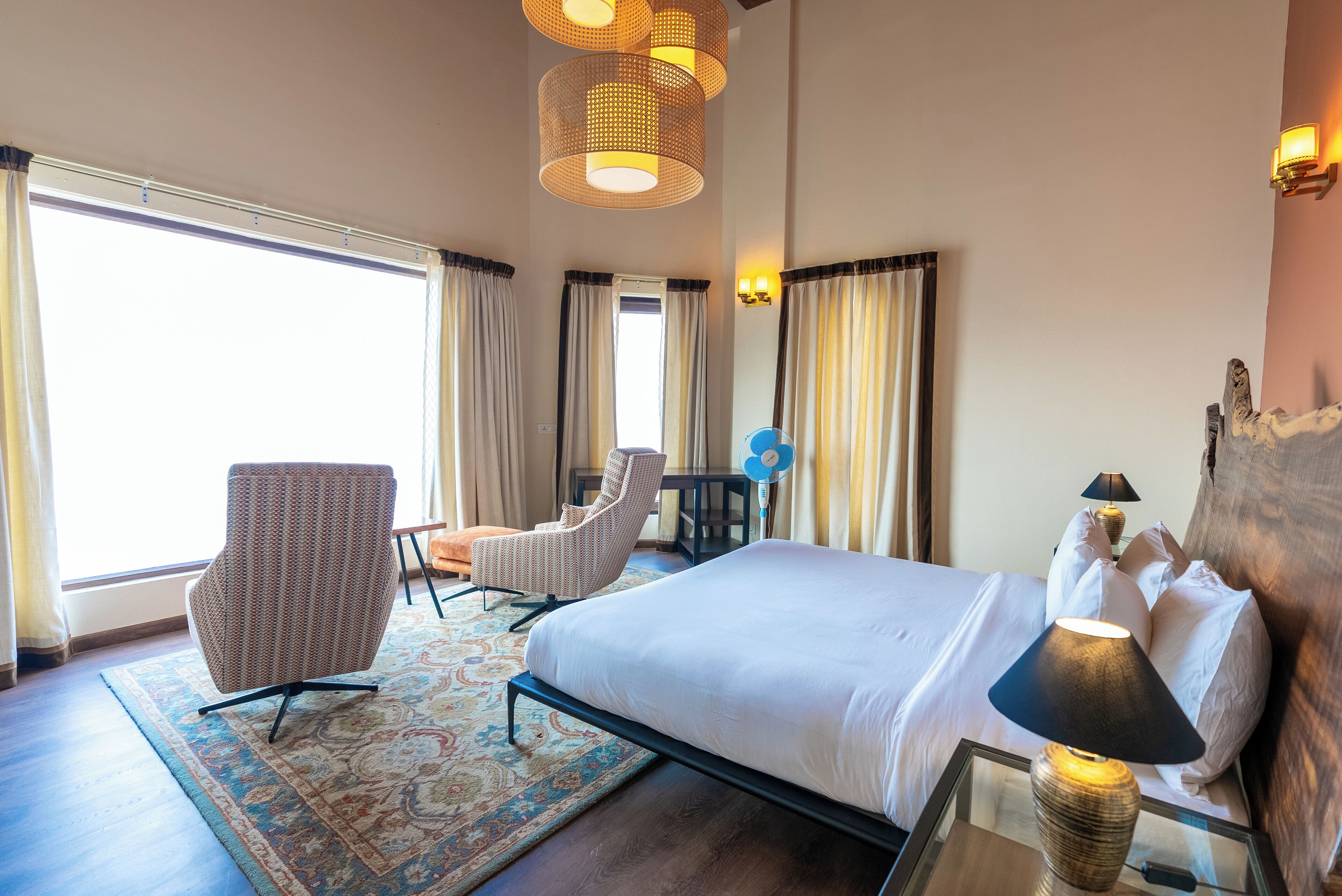 A hotel room with a large bed, two armchairs, a desk, and a window with curtains.