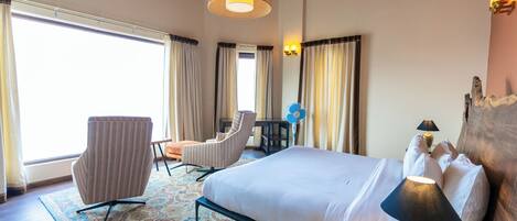 A hotel room with a large bed, two armchairs, a desk, and a window with curtains.