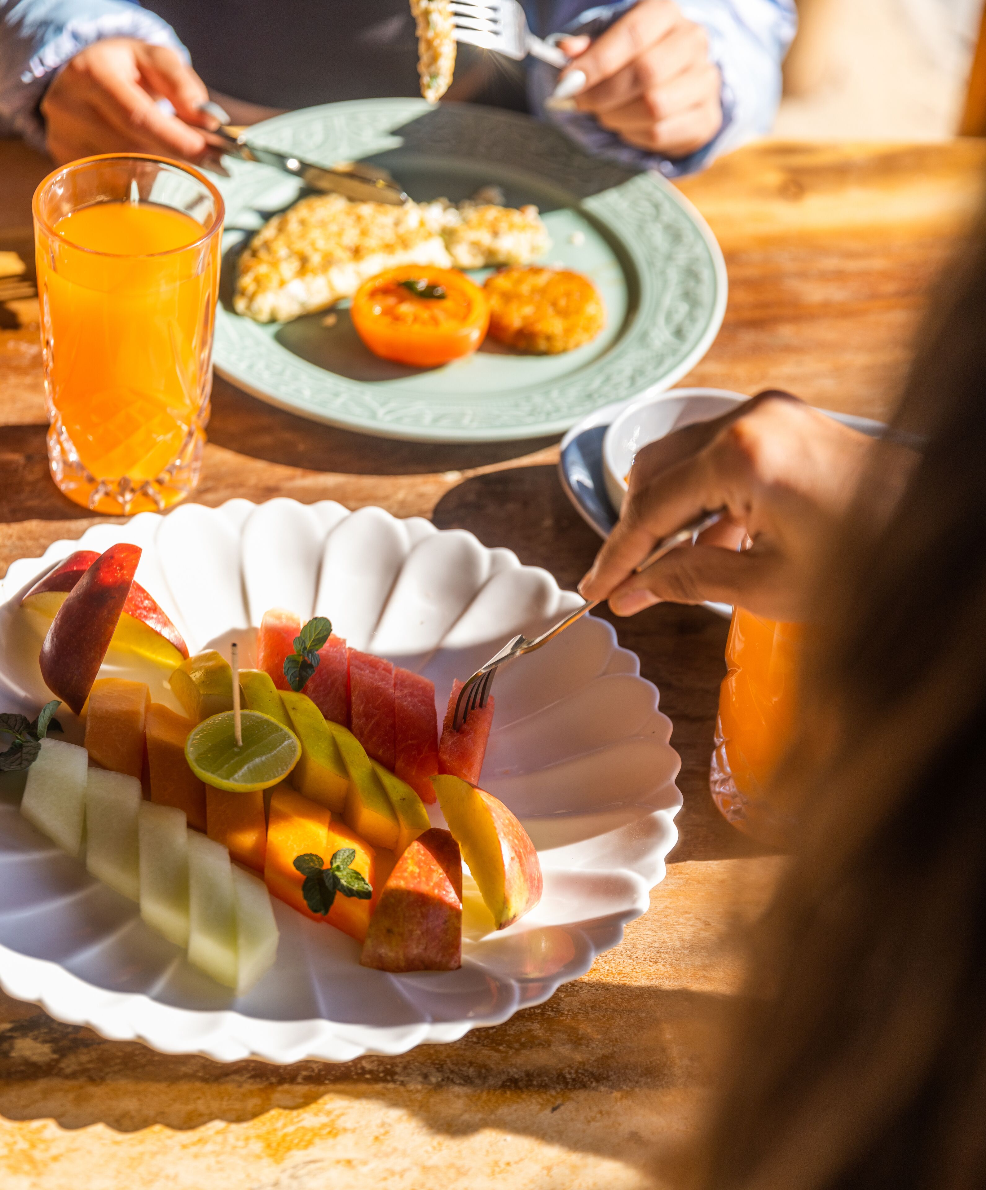 A breakfast setting with a plate of fruit, a glass of orange juice, and a green plate with toast.