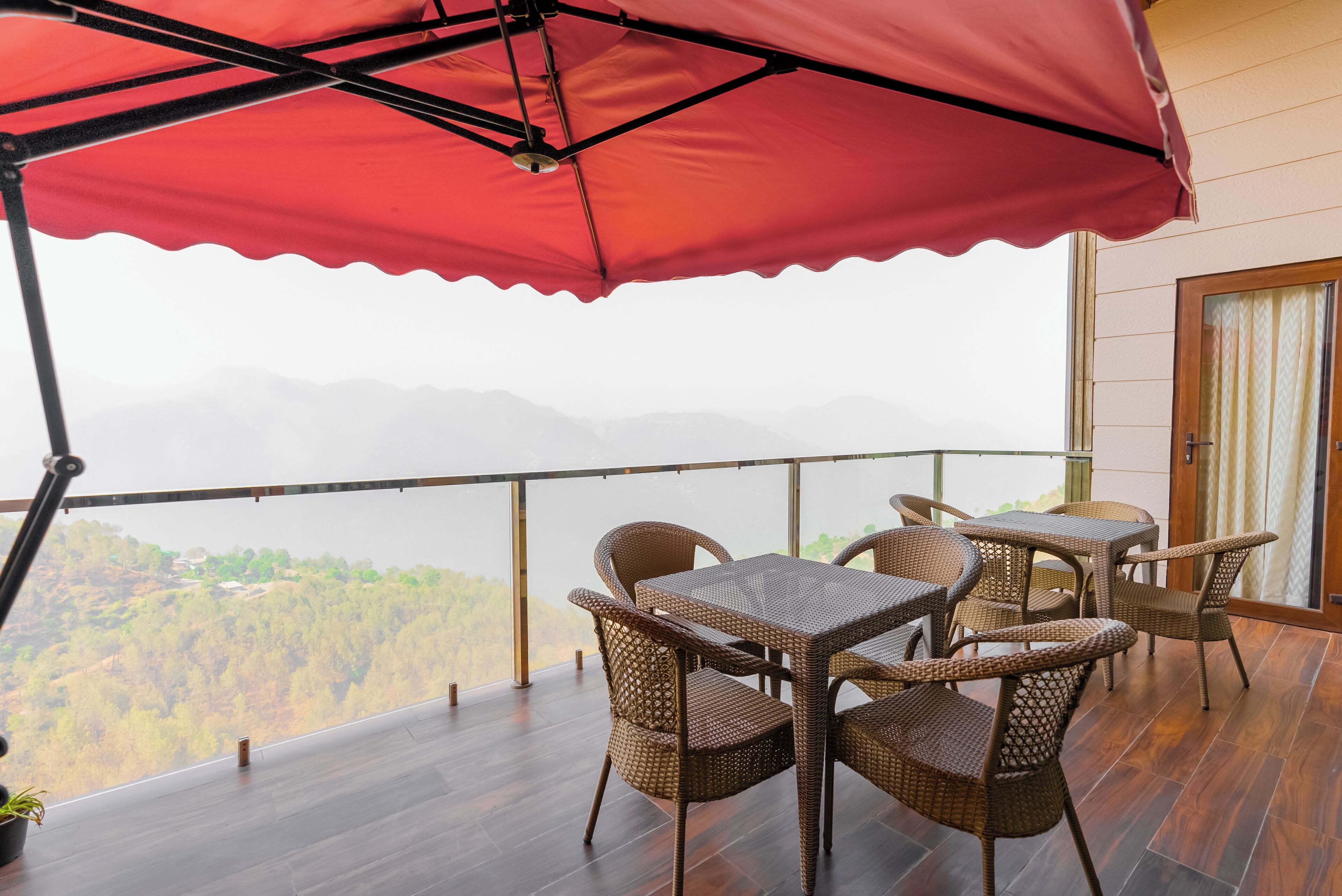 A balcony with wicker furniture and a red canopy, overlooking a mountainous landscape.