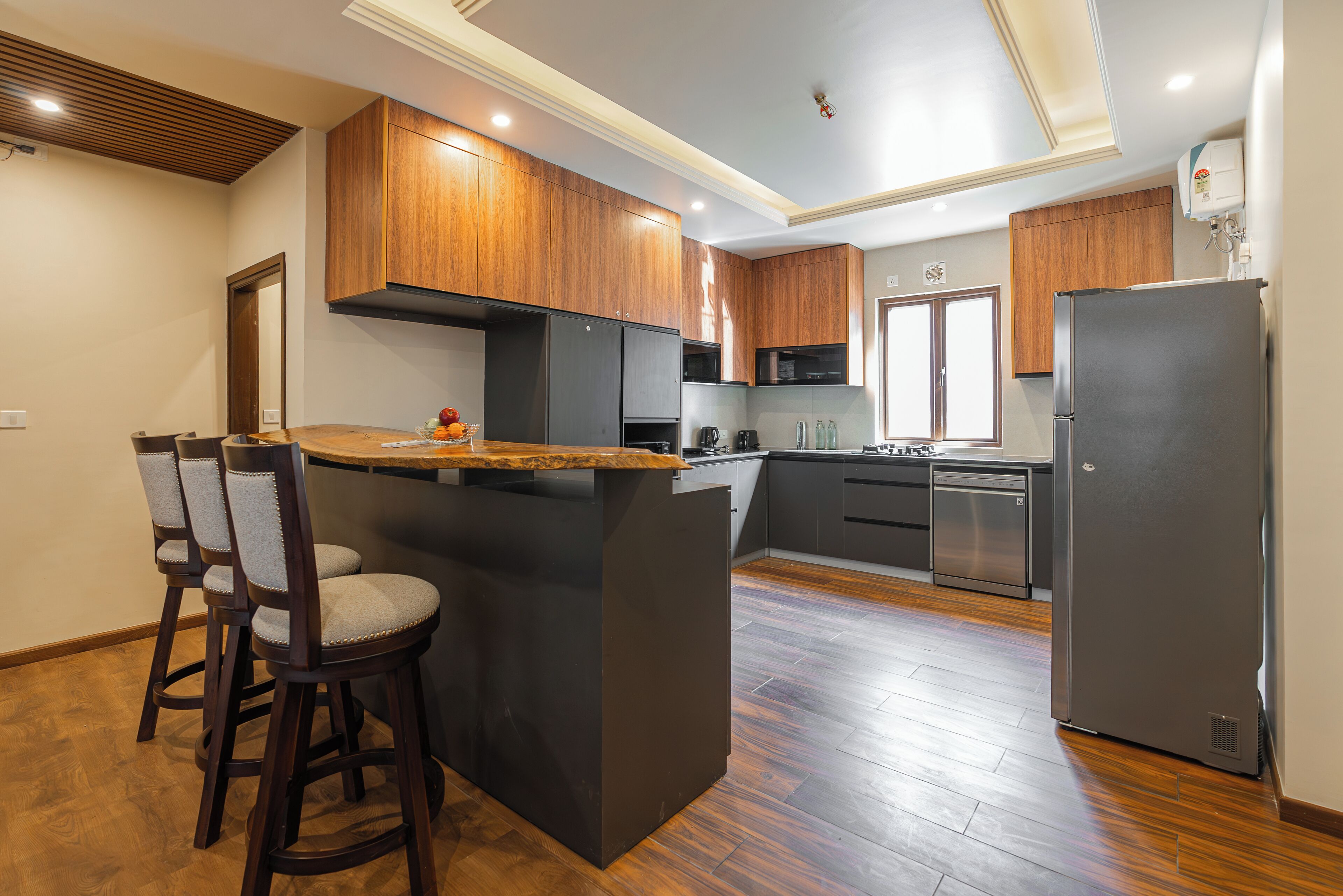 Una cocina moderna con armarios de madera, una isla central con taburetes de bar, un refrigerador y un lavavajillas.