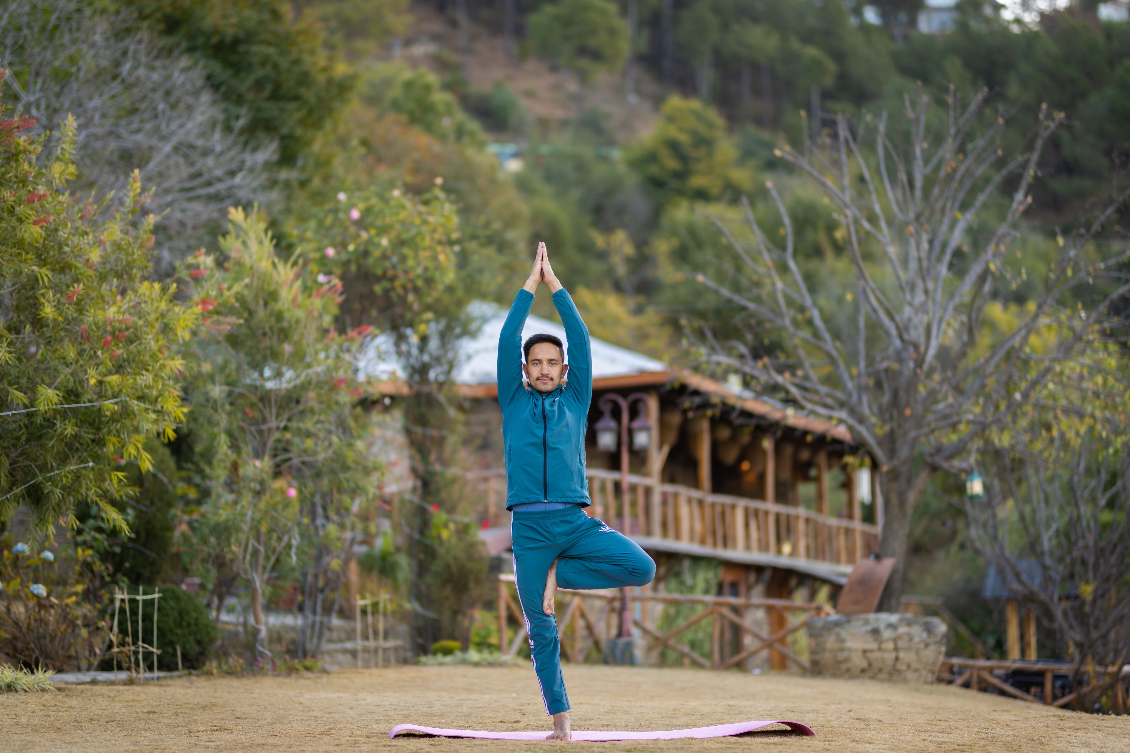 A person performing a yoga pose outdoors with a wooden cabin in the background.