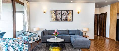 En moderne stue med en grå modulsofa, et rundt sofabord og lænestole med blomstermønster. To vægmonterede lamper og et stort abstrakt maleri hænger over sofaen.