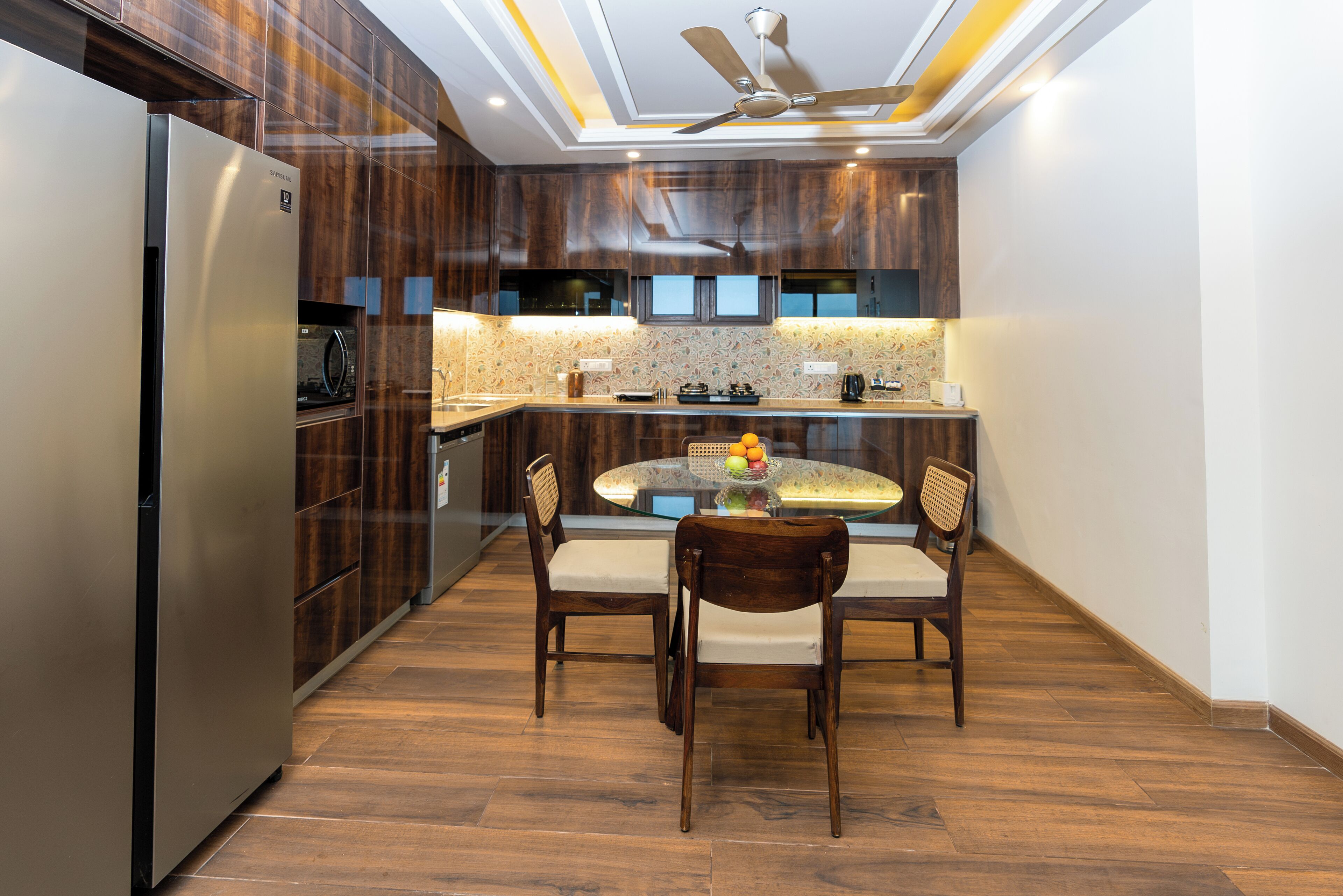 Cocina moderna con gabinetes de madera oscura, un refrigerador de acero inoxidable, una mesa de comedor con cuatro sillas y un ventilador de techo.