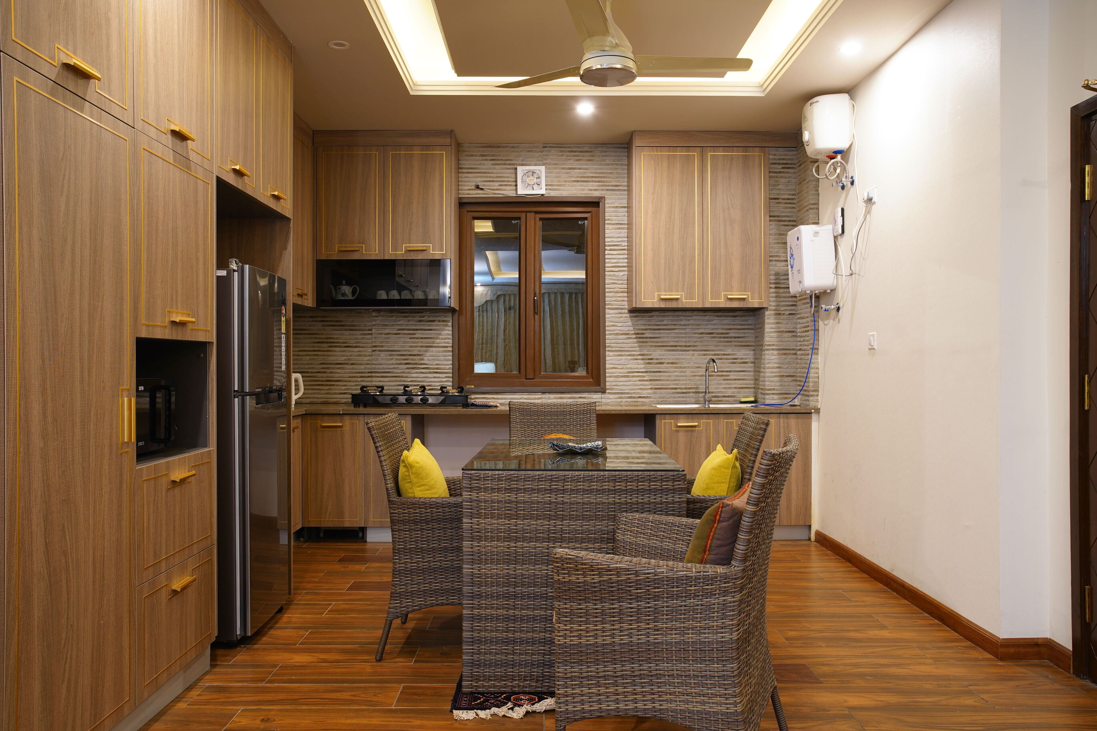A modern kitchen with wooden cabinets, a stainless steel refrigerator, a dining table with wicker chairs, and a ceiling fan.