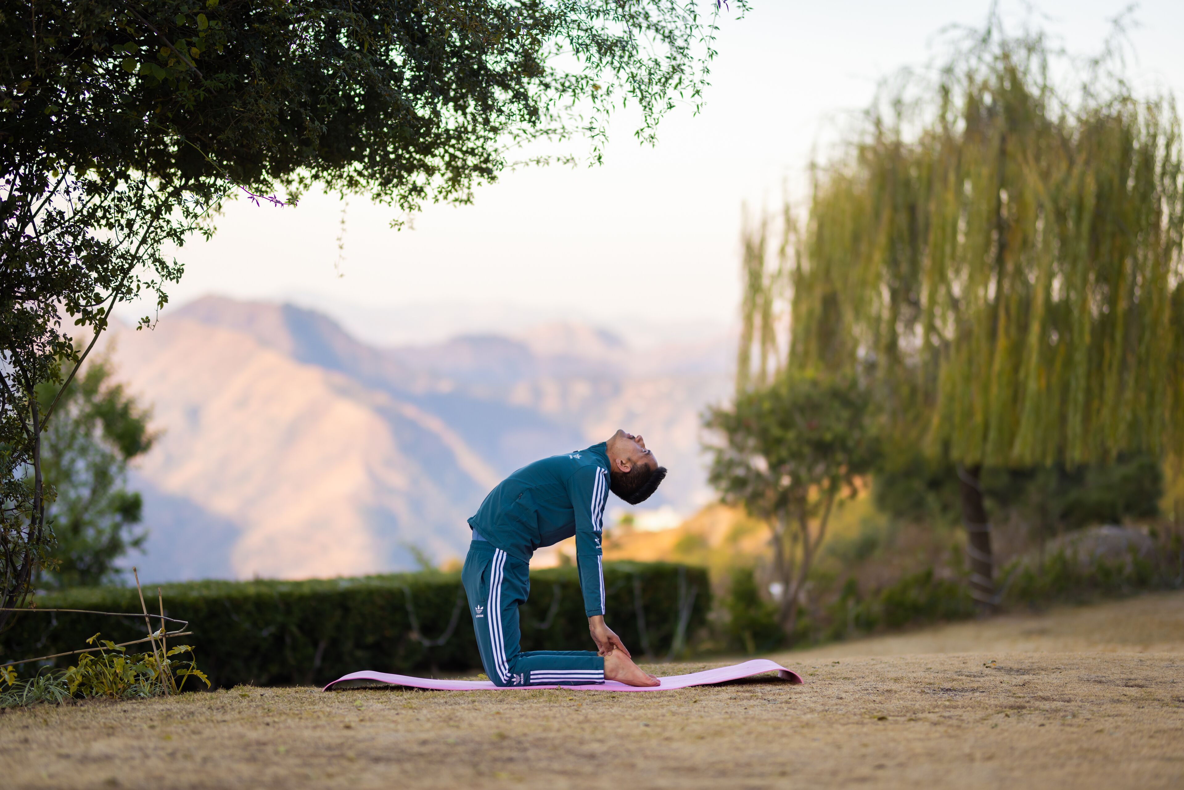 Une personne effectue une posture de yoga sur un tapis, à l'extérieur, avec un paysage montagneux en arrière-plan.