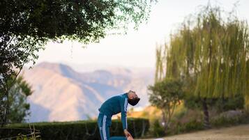 Une personne effectue une posture de yoga sur un tapis, à l'extérieur, avec un paysage montagneux en arrière-plan.