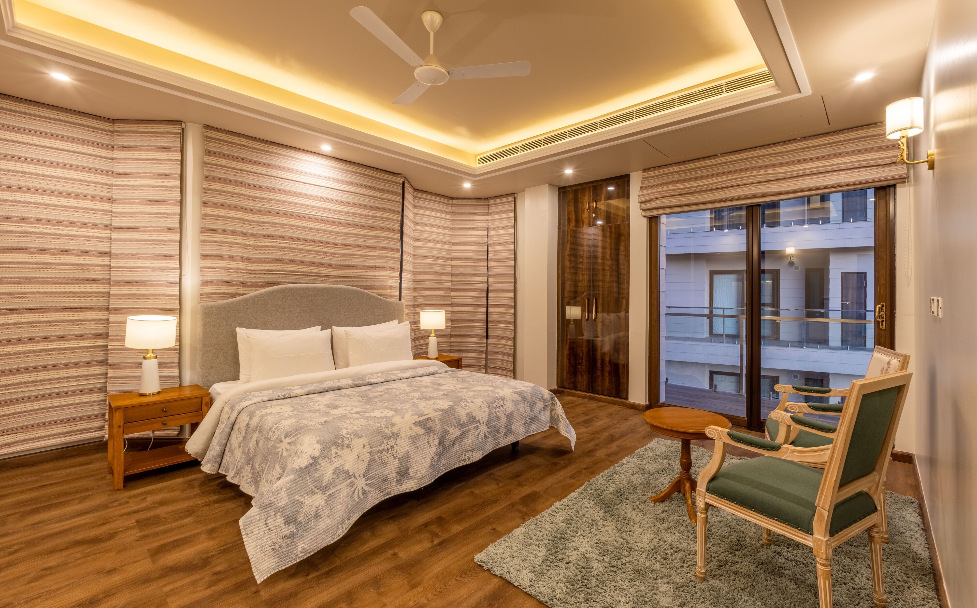 A modern bedroom with a large bed, a ceiling fan, and a view of a building through a glass door.