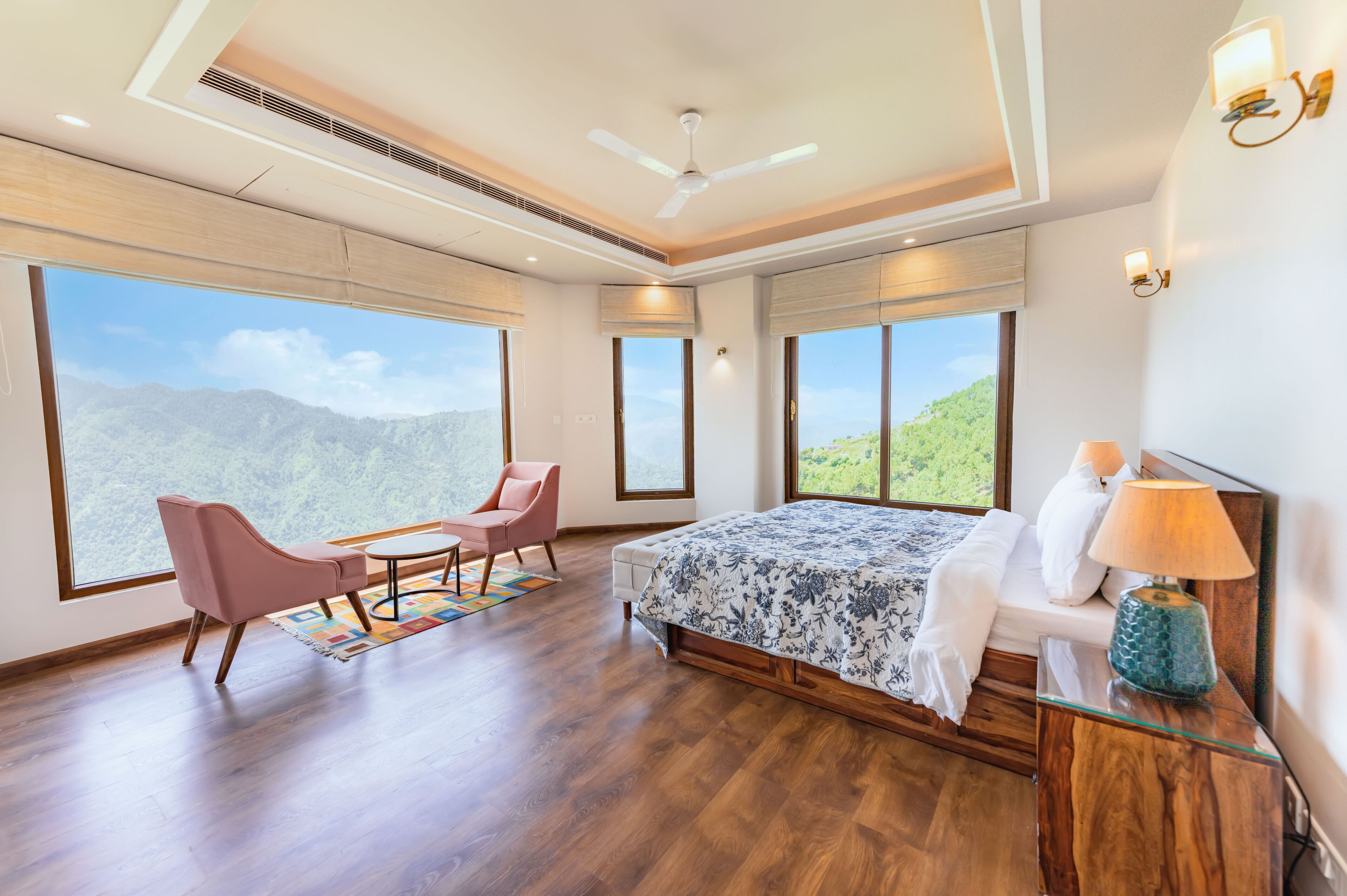 A bedroom with a large bed, a chair, a small table, and a view of mountains through large windows.