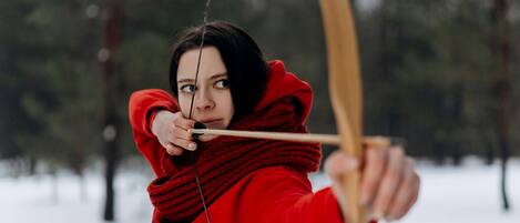 A person in a red jacket aiming a bow in a snowy forest.