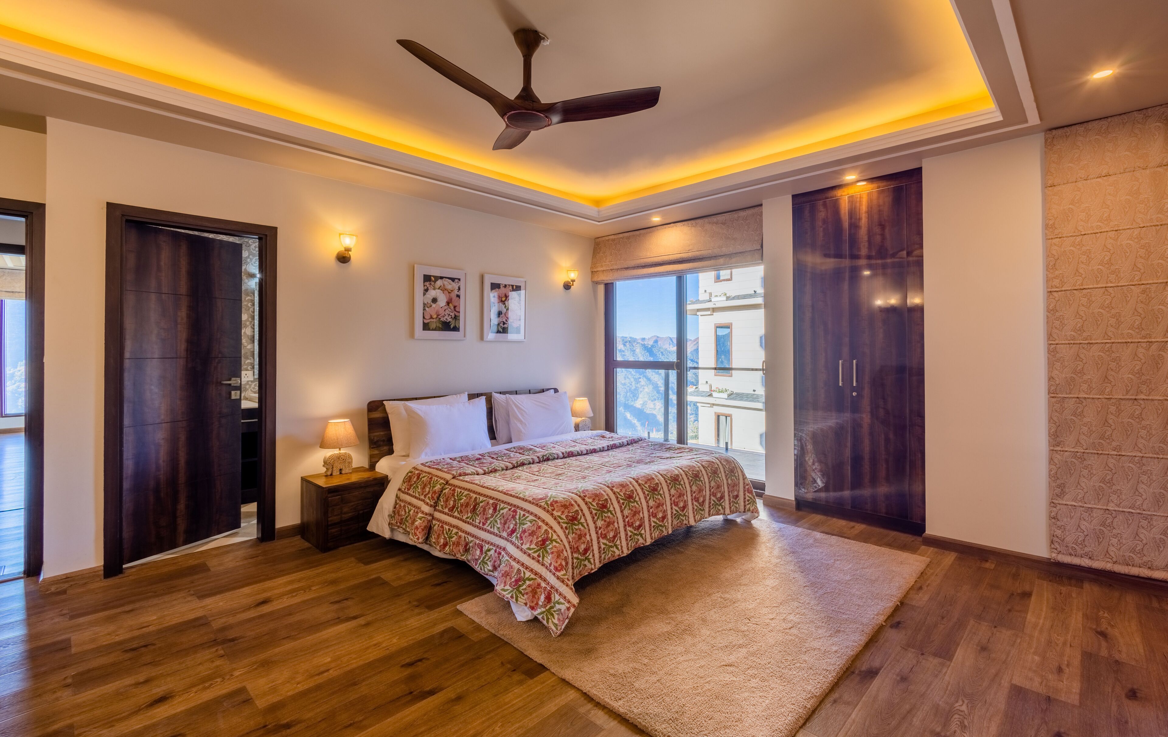 A bedroom with a bed, a ceiling fan, a large window, and a wardrobe.