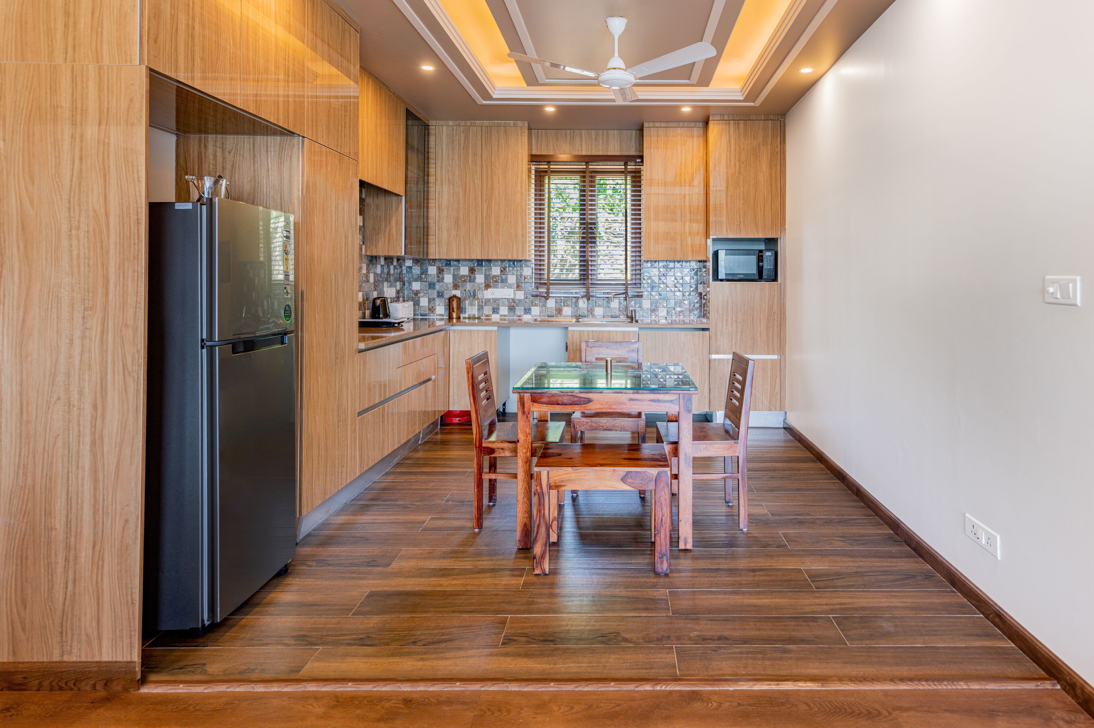 A modern kitchen with wooden cabinets, a black refrigerator, a glass dining table, and a ceiling fan.
