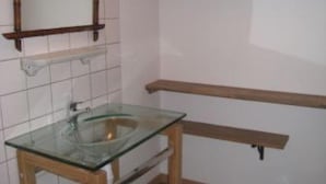 Een badkamer met een glazen wastafel, houten planken en een spiegel.