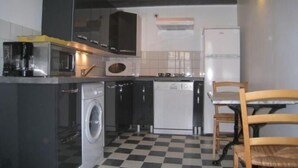 Een compacte keuken met een wasmachine, magnetron en een klein eethoekje met een stoel.
