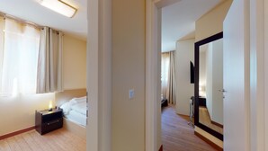 A hotel room with a bed, bedside table, lamp, and a mirror. - Modern 3½-room apartment on the ground floor, approx. (Madulain)