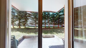 A patio area with a concrete floor, surrounded by trees and a view of the sea. - Modern 3½-room apartment on the ground floor, approx. (Madulain)