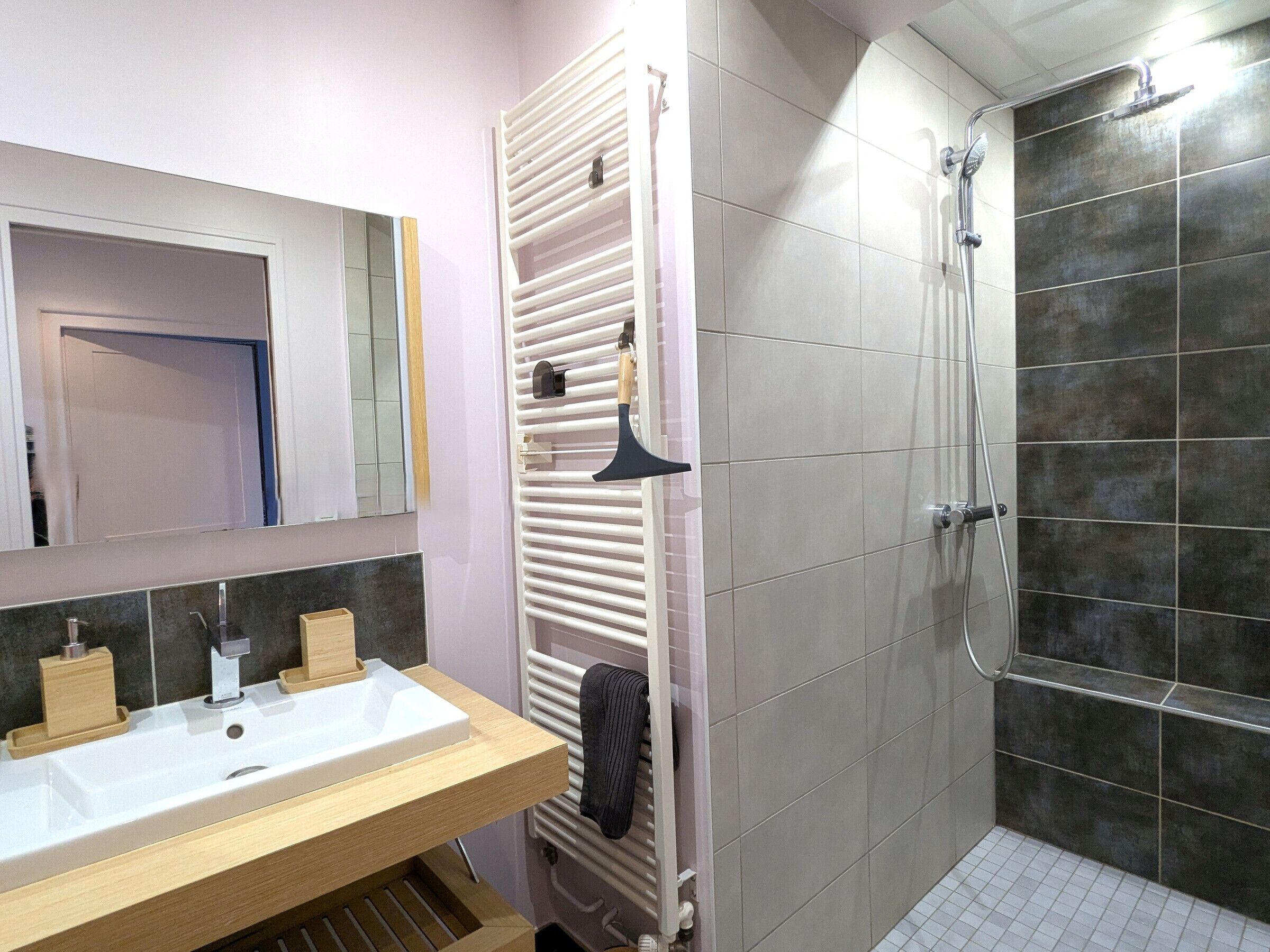 Une salle de bain équipée d’un lavabo, d’un miroir, d’un porte-serviettes, d’une douche et d’un radiateur.