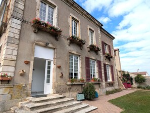 Un edificio histórico con fachada de piedra, varias ventanas con contraventanas y jardineras en los pisos superiores.