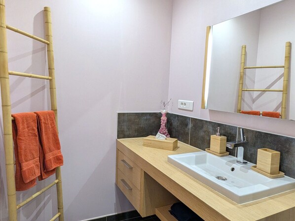 Un baño con tocador de madera, dos lavamanos, un espejo y una escalera de bambú con toallas naranjas.