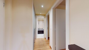 A narrow hallway with wooden flooring leading to a kitchen area with a sink and cabinets. - Modern 3½ room flat on the ground floor, approx. (Madulain)